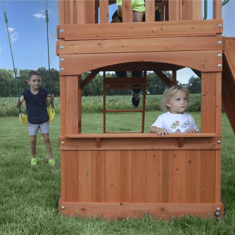 Children playing on Atlantis Cedar Wood Swing Set With Wave Slide And Raised Clubhouse Featuring Rock Wall, Belt Swings, Balcony.