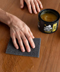 Real Deal Plant Based Furniture Butter With Slick Paste Wax Wood Finish curing on a wooden table with a hand applying wax using a sponge.