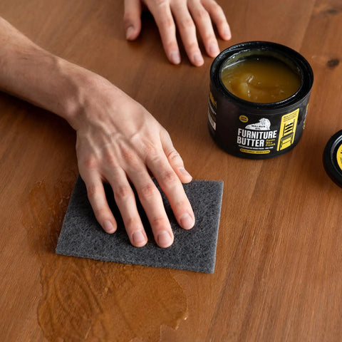 Real Deal Plant Based Furniture Butter With Slick Paste Wax Wood Finish curing on a wooden table with a hand applying wax using a sponge.