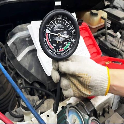 Front view of a black HFS fuel pump tester gauge with white dial, held by a gloved hand under the hood.