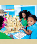 Children building a detailed wooden puzzle house model in a classroom setting.