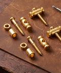 Premium Brass Electric Guitar String Trees Retainers 2 Pairs on leather background, includes screws and mounting parts for tuner heads.