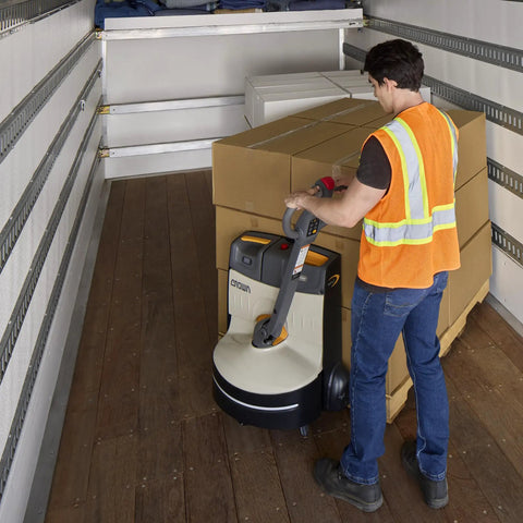 Man using Compact Crown Wj 50 Electric Pallet Jack With Lithium Battery for hauling stacked boxes in a truck.
