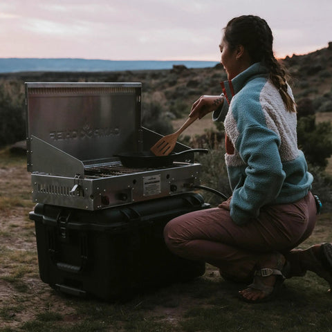 Person cooking on a Trail 80 Waterproof Storage Box With Wheels, 79L Outdoor Gear Case used as a table in a camping setting.