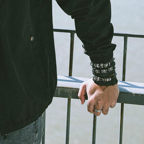Badass Six Piece Braided Leather Bracelet Set For Men And Women Adjustable Hemp Rope Wristbands With Classic Skull Charm Punk Rock Style Fresh Daily Bling worn by a person resting on a railing.