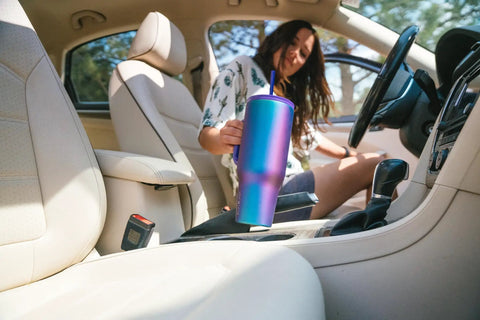 Woman placing Co Pilot Insulated Travel Mug With Straw And Flip Cap Lids 40 Oz Leak Proof Cup Holder Friendly in car, Aurora color.