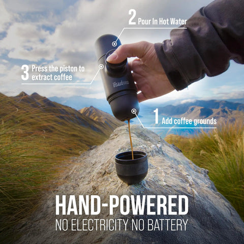 Hand using Minipresso GR Portable Espresso Machine For Ground Coffee, Manual Hand Press Coffee Maker in a mountain setting