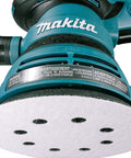 Close-up of five-inch random orbit sander with 8-hole sanding disc attached, part of the Multi Grit 30 Piece Five Inch Random Orbit Sanding Disc Set With Eight Hole Hook And Loop Includes 10 Of Each 80 120 240 Grit Discs For Wood Metal Drywall And More A DIY Ready Must Have For Heavy Material Removal And Smooth Finishes.