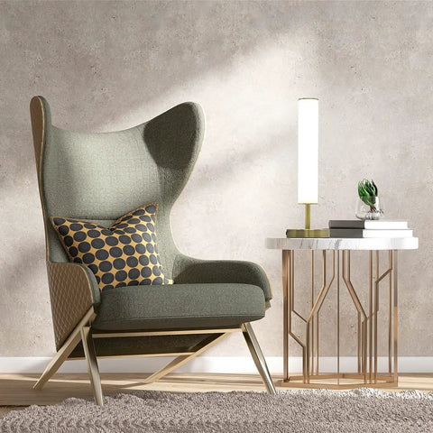 Chill Minimalist LED Cylinder Lamp With USB Charge Port 360 Degree Glow Three Color Temperatures Dimmable Desk Or Night Lamp For Living Room Bedroom Or Home Office In Antique Brass on a side table next to a green chair.
