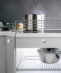 Stainless steel pot on a modern kitchen stove with brushed nickel cabinet knobs and a silver colander underneath.
