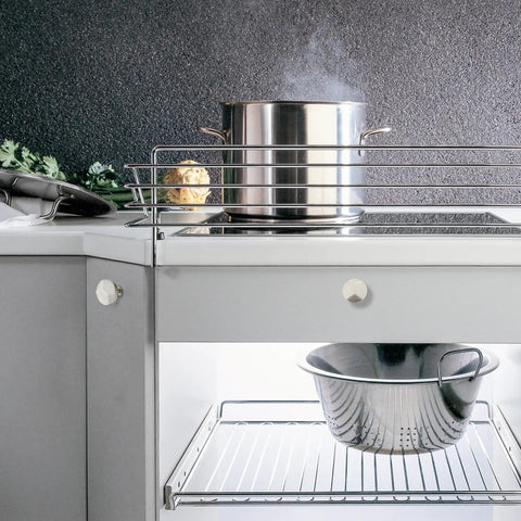 Stainless steel pot on a modern kitchen stove with brushed nickel cabinet knobs and a silver colander underneath.