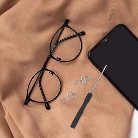 Glasses repair kit with eyeglasses, screwdriver, and screws on brown fabric, showcasing components for easy spectacle maintenance.