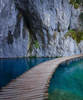Curved wooden path crossing turquoise water next to a rocky cliff