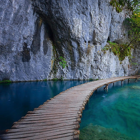 Curved wooden path crossing turquoise water next to a rocky cliff
