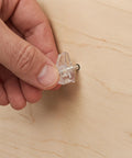Hand inserting Clear Plastic Shelf Pegs With Studs 60 Pack Lightweight No Fuss Cabinet Pins into wooden surface