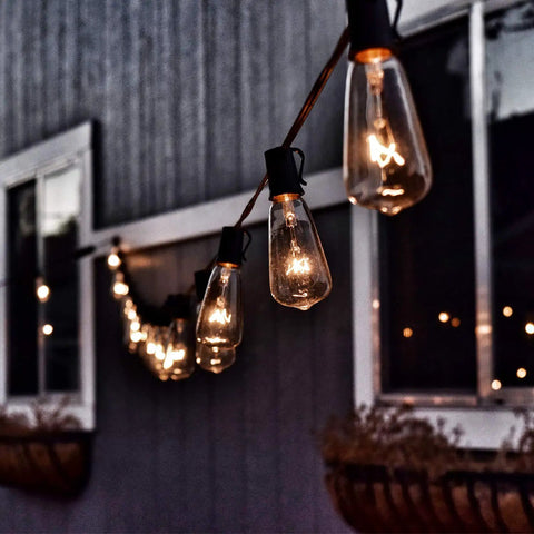 25 Pack Edison Style Replacement Light Bulbs 7-Watt E12 Candelabra Base ST40 Clear Glass Warm White 2300K Ideal For Outdoor Patio String Lights Waterproof And Rust Resistant illuminating a patio space at dusk.