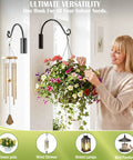 Heavy Duty Plant Hanger Bracket 16 Inch Black Outdoor Hand Forged Metal Hanging Bracket With 80 Lbs Capacity For Plants And Bird Feeders Built To Last Rock Solid Stable Weatherproof And Rust Resistant mounted on wall with flower pot and wind chimes.