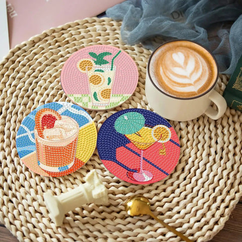 Three diamond-painted cocktail coasters on a wicker surface with a latte, part of the Eight Piece Diamond Art Coaster Kit With Holder For DIY 5D Retro Cocktail Coasters Diamond Painting Set For Adults And Beginners Includes Adhesive Cork Bases Diamond Tiles And Marker Pen.