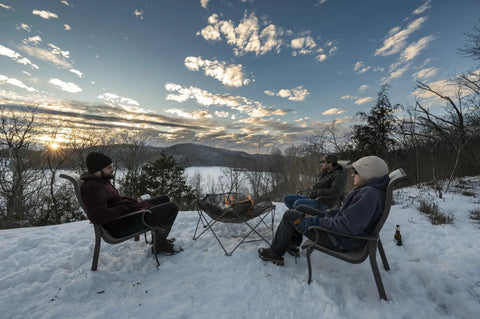 Three people seated around Gaze Fire Pit Portable Stainless Steel Mesh Outdoor Fire Pit With Ground Heat Shield in snowy landscape
