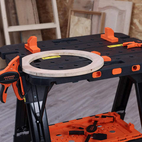 4 Pack Clamp Dogs Kit For Portable Folding Work Table on black table with orange clamps and wooden ring, shop background