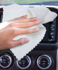 White microfiber cleaning cloth wiping a car dashboard touchscreen and control panel.