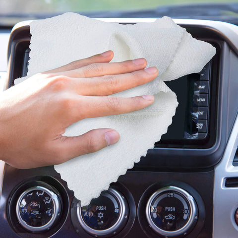 White microfiber cleaning cloth wiping a car dashboard touchscreen and control panel.