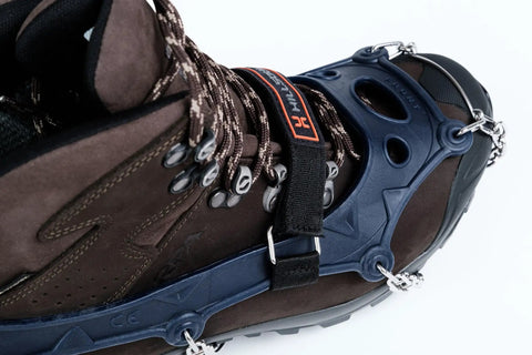 Trail Crampon Ultra I Ice Cleat Traction System attached on a brown hiking boot, showing heat treated stainless steel spikes