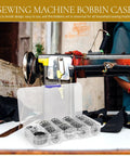 Must Have 31 Piece Bobbin And Small Bobbin Case Set For Household And Industrial Sewing Machines, Easy To Install, Prevents Knots And Unraveling, Portable Crafting And Repair Kit For Everyday Sewing Projects. Clear plastic box with silver metal bobbins and a bobbin case beside a sewing machine.