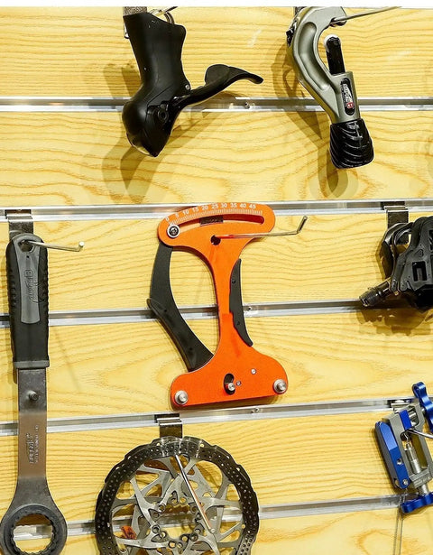 Orange Bike Spoke Tension Meter And Spoke Wrench Kit for Road And Mountain Bikes displayed on a wooden wall.