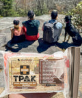 Mini T PAK Trail First Aid Kit For Backpacking And Camping with hikers and dog in background on rocky overlook.