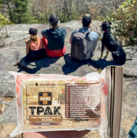 Mini T PAK Trail First Aid Kit For Backpacking And Camping with hikers and dog in background on rocky overlook.