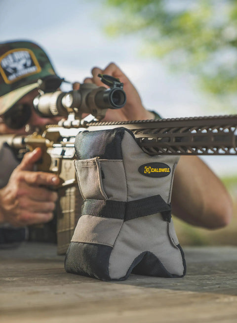 Tactical DeadShot Front And Rear Rifle Rest Combo on table with shooter aiming, filled and range ready, heavy duty ballistic nylon.