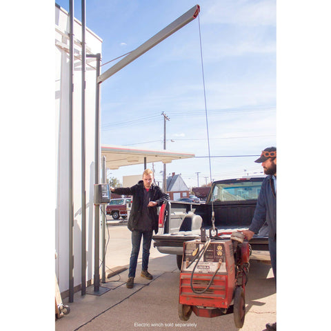 Blue winch cable with hook attached to a tall outdoor hoist beside a pickup truck.
