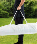 Person carrying a white carry bag for a 10x20 Outdoor Party Tent Canopy With Removable Walls in a grassy backyard.