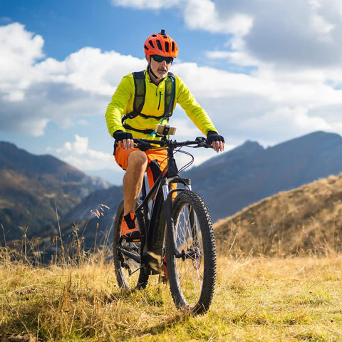 Cyclist riding a mountain bike on grassy terrain, showcasing durable tires for Two Pack Heavy Duty Bike Tire Inner Tubes 26 By 1 3 Eighths Inches AV32mm Schrader Valve 37-590 ETRTO Compatible Replacement Tubes For 26 By 1 3 Eighths Inches Wheels Ride Ready Tough As Nails.