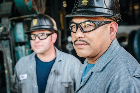 Workers wearing safety glasses and hard hats in an industrial setting.