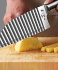 Kitchen crinkle cutter knife with stainless steel wavy blade cutting potatoes on a wooden cutting board