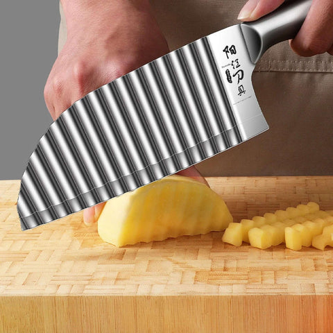 Kitchen crinkle cutter knife with stainless steel wavy blade cutting potatoes on a wooden cutting board