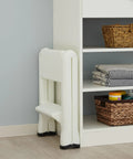Two Step Folding Foot Stool, 14 Inch High, 300 Pound Capacity, folded near shelf in modern room, lightweight and compact design