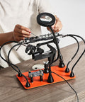 Magnetic Helping Hands Soldering Station With Four Arms Vise LED Magnifying Lamp on table, person adjusting components.
