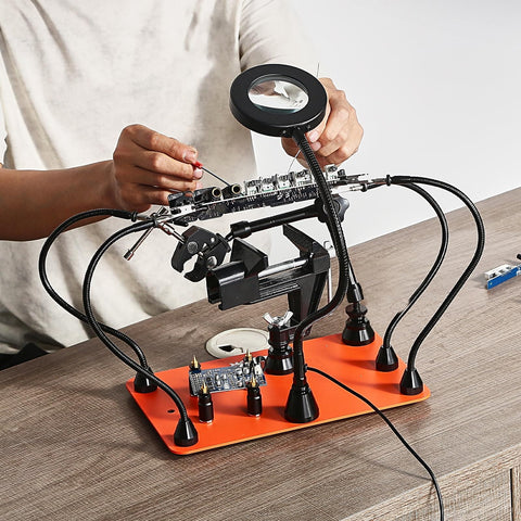 Magnetic Helping Hands Soldering Station With Four Arms Vise LED Magnifying Lamp on table, person adjusting components.
