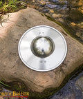 Old School Medieval Steel Buckler Shield Handcrafted With Wooden Grip on rock by stream, 30 cm, 16-gauge, polished finish