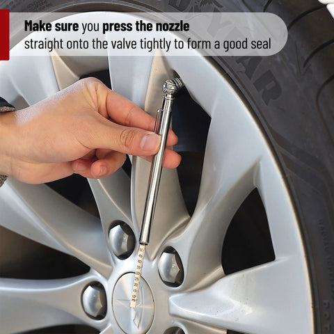 Chrome pencil tire gauge held to a car tire valve; slim metal body with measurement scale.