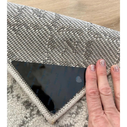 Hand applying No Slip Rug Grippers 12 Pack Carpet Stickers For Area Rugs Double Sided Tape For Hardwood Floors And Tile Floors No Damage Anti Slip Fasteners Stop Rug Pad Curling And Slipping under a rug corner.