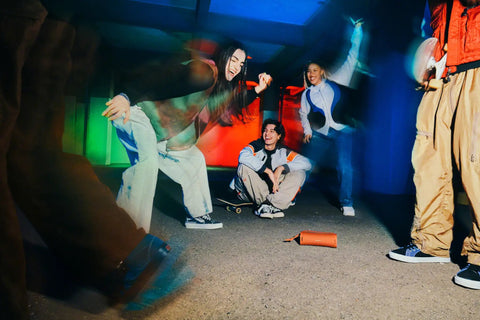 Group of friends enjoying music outdoors with the Ultimate Field 1 Waterproof Portable Bluetooth Speaker on the ground, colorful lights.
