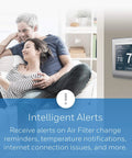 Couple on couch with WiFi Color Thermostat With 7 Day Programmable Schedule Touch Screen shown on wall, gray finish, smart alerts displayed.