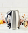 Stainless Steel Electric Kettle 1.7 Liter Cordless Design With 1500 Watt Power boiling water beside tea and lemon on counter.