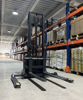 Heavy Duty Electric Straddle Stacker 3300 Lb Capacity in warehouse aisle with pallets in background, showcasing lift and wheels.