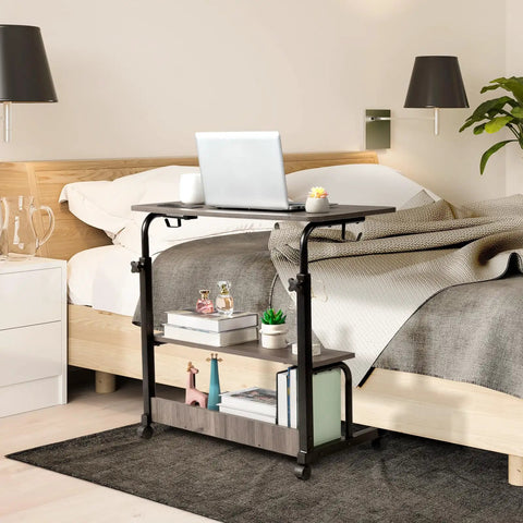 Unwind And Handle Daily Grind At This Grey Oak Rolling Standing Desk With Height Adjustable Top Smooth Gliding Wheels Grab And Go Mobility Side Hooks And Roomy Storage Shelves For Your Home Office Setup, compact desktop with laptop on rolling cart beside bed.