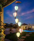 Solar Powered Wind Chimes With Hot Air Balloon Lights For Outdoors Auto Light Up Garden Decor at sunset in a backyard setting.